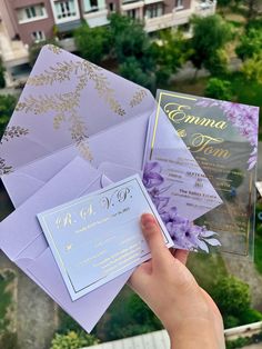 someone holding up some purple and gold wedding cards