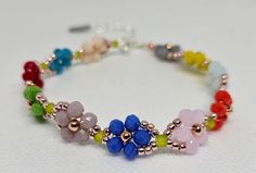 a bracelet with multi colored beads and flowers on the clasp is sitting on a white surface