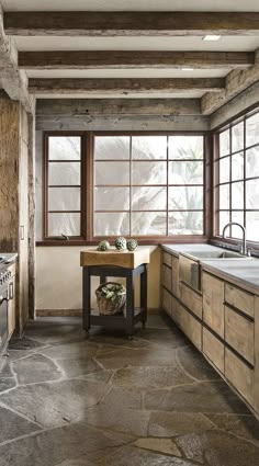 a kitchen with stone flooring and wooden cabinets in the corner, next to an open window