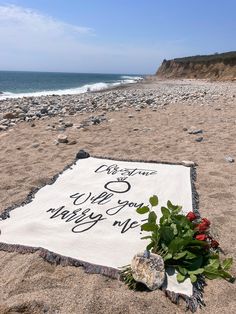 a white blanket with writing on it sitting on top of a sandy beach next to the ocean