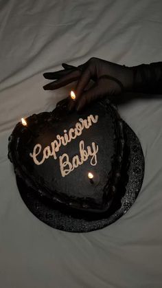 a heart shaped cake with the words capricon baby on it and lit candles