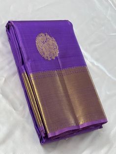 a purple and gold sari with a lion on the front is laying on a white sheet