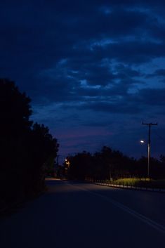 an empty street at night with the lights on and dark clouds in the sky above