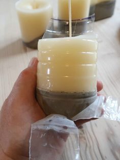 a person holding a candle in front of some candles on a table with plastic wrap around it