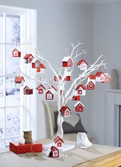 a white tree with red and white houses hanging from it's branches in front of a window