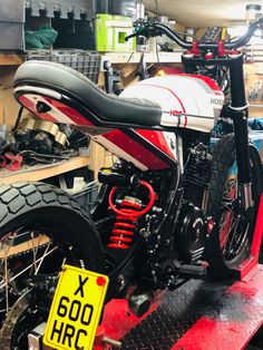 a red and white motorcycle parked on top of a wooden platform in a garage next to other motorcycles