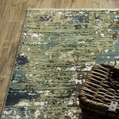 a woven basket sitting on top of a wooden floor next to a rug covered in multicolored paint