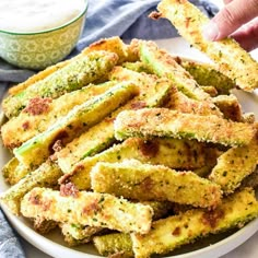 someone is dipping something into a white plate with some fried zucchini on it