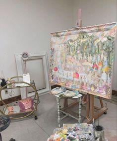 an artist's easel with paintings on it in a room filled with other items