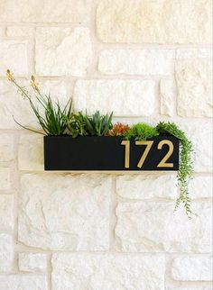 a black and gold house number sign mounted to a brick wall with succulents