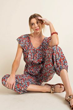 A comfortable jumpsuit with a pop of red and sprinkle of flowers. This jogger style jumpsuit has an elastic waistline, shaping the loose, lightweight fabric. There is a ruffled fabric detail along the neckline and sleeves, and side pockets. Style with sandals for a picnic in the park. Model is 5'10" and wearing her true size Small. Small: Bust 18", Length 54.5" 100% Rayon Casual Floral Print V-neck Jumpsuits And Rompers, Casual Printed V-neck Jumpsuits And Rompers, Summer Floral Print Red Jumpsuits And Rompers, Red Floral Print Jumpsuits And Rompers For Summer, Casual Multicolor Jumpsuits And Rompers With Elastic Waistband, Casual Jumpsuits And Rompers With Elastic Waistband For Vacation, Red Floral Print Jumpsuit With V-neck, Casual Jumpsuits And Rompers With Elastic Waistband, Casual Red V-neck Jumpsuits And Rompers