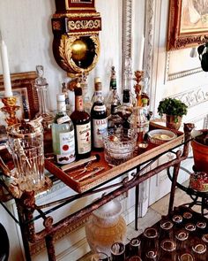 there are many bottles and glasses on the bar cart in front of the wall mirror