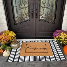 a front door with a welcome mat, pumpkins and flowers on the ground next to it