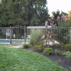 a fenced in pool area next to a lush green yard with flowers and trees