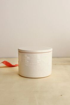 a white canister sitting on top of a wooden table next to a red ribbon