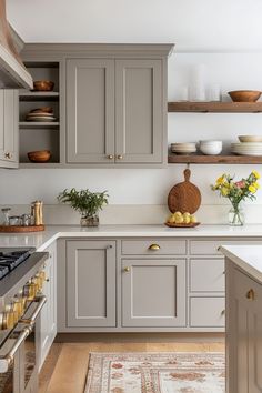 a kitchen with gray cabinets and white counter tops, yellow flowers in vases on the stove