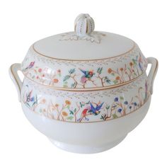 a white bowl with floral designs on the rim and lid is sitting in front of a white background