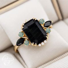 a black stone surrounded by green and white stones in a gold tone ring with diamond accents