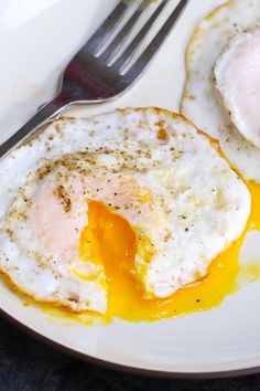 two fried eggs are on a plate with a fork