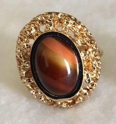 Beautiful vintage Karatclad and polished stone ring from our 1980's collection that are new, never worn and in excellent condition. The ring measures 7/8" long x 3/4" wide with the stone measuring 15x10mm.  The colors vary with each piece but are each a shade of brown from light to dark. Vintage Jewelry With Large Stone In Open Ring, Vintage Moonstone Oval Cabochon Ring, Vintage Oval Cabochon Moonstone Ring, Retro Handmade Oval Jewelry, Vintage Gemstone Rings For Collectors, Vintage Round Cabochon Rings, Vintage Cabochon Round Rings, Adjustable Retro Ring, Retro Adjustable Ring