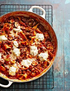 a large pot filled with pasta and meat on top of a cooling rack next to a wooden table