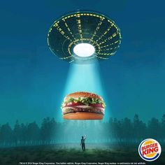 a man standing in front of a giant hamburger under a light that is shining down