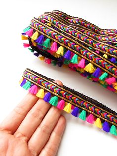 a hand is holding two pieces of colorful beaded bracelets with tassels