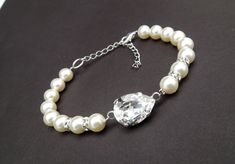 a white bracelet with pearls and a crystal bead on the clasp is sitting on a black surface