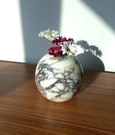 a marbled vase with flowers in it on a wooden table next to a window