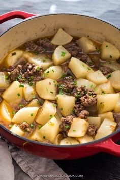 a pot filled with meat and potatoes sitting on top of a wooden table next to a cloth