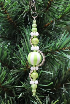 a green and white beaded ornament hanging from a christmas tree with pine needles