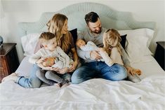 a man and woman sit on a bed with their two children, who are holding baby dolls