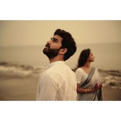 two people are standing on the beach looking up at the sky and one is wearing a white shirt