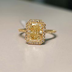 a fancy yellow diamond ring sitting on top of a white surface with diamonds around it