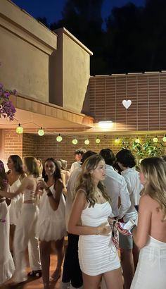 a group of people standing around each other in white dresses and one man is holding a cell phone