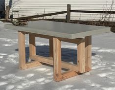 a table sitting in the middle of snow covered ground next to a fence and house