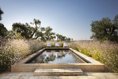 an outdoor swimming pool surrounded by trees and flowers with two lounge chairs on the side