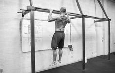 a shirtless man is hanging upside down on a bar in a crossfit gym