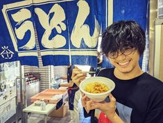 a man holding a bowl of food in front of him and smiling at the camera