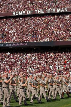 a group of men in uniform marching on a field with people watching from the stands