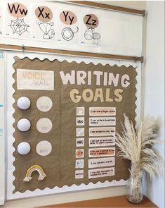 a bulletin board with writing goals written on it next to a vase filled with dry grass