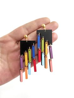 a pair of multicolored earrings is being held by a hand