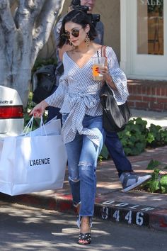 a woman walking down the street carrying shopping bags and holding a drink in her hand