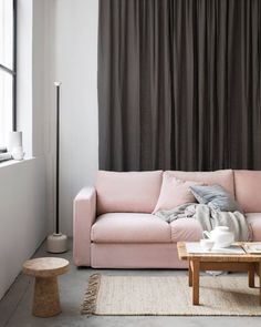 a living room with a pink couch and coffee table in front of a curtained window