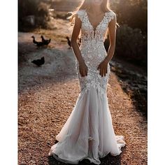 a woman in a wedding dress standing on a dirt road with birds around her and the sun behind her