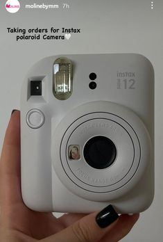 a person holding up a white camera in front of the camera with an instax sticker on it