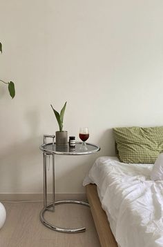 a bedroom with a bed, table and plant on the floor next to each other