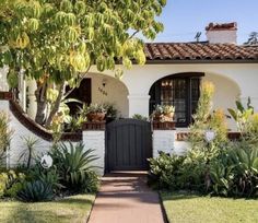 a white house with lots of plants and trees around it's front entrance area