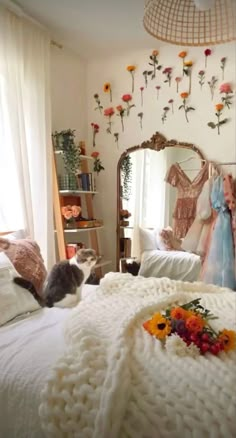 there is a cat laying on the bed in front of a mirror with flowers hanging from it