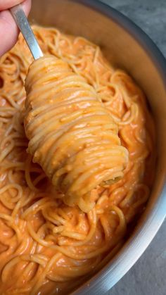 a hand holding a fork over a bowl of noodles